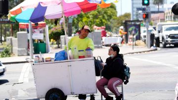 A street vendor selling snow cones tends to a customer at a street corner near MacArthur Park, Tuesday, July 11, 2023, in Los Angeles. (AP Photo/Marcio Jose Sanchez)