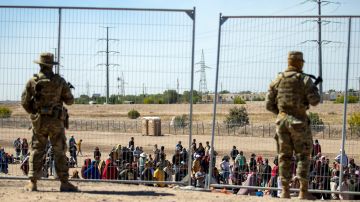 ARCHIVO - Migrantes esperan junto a una valla fronteriza bajo la vigilancia de la Guardia Nacional de Texas el 10 de mayo de 2023 para ingresar a El Paso, Texas. (AP Foto/Andrés Leighton)