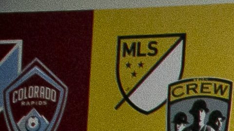 Don garber, comisionado de la MLS junto al logo de la liga y de algunos equipos.