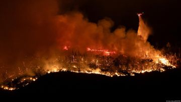 Un helicóptero lanza agua sobre el incendio forestal Thompson mientras los bomberos siguen luchando contra el fuego en la noche cerca de Oroville, California.