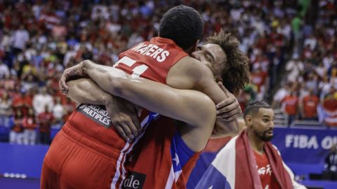 Puerto Rico's George Conditt IV, center, and Arnaldo Toro, embrace after their team qualified for the Paris 2024 Olympics after eliminating Lithuania in a FIBA Olympic Qualifying basketball final in San Juan, Puerto Rico, Sunday, July 7, 2024. (AP Photo/Alejandro Granadillo)