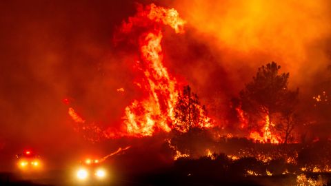 Las llamas saltan por encima de los vehículos de bomberos cuando el incendio de Park cruza la autopista 36 en el condado de Tehama el 26 de julio de 2024.