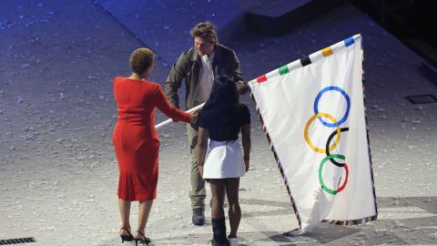 La alcaldesa de Los Ángeles, Karen Bass y la gimnasta Simone Biles, entregan la bandera olímpica al actor estadounidense Tom Cruise.