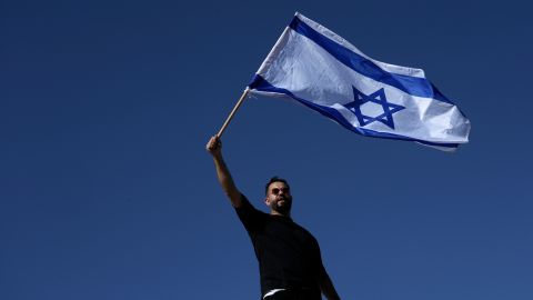 A protester waves the Israeli national flag in support of soldiers being questioned for detainee abuse, outside of the Sde Teiman military base, Monday, July 29, 2024. The Israeli military said Monday it was holding nine soldiers for questioning following allegations of "substantial abuse" of a detainee at a shadowy facility where Israel has held Palestinian prisoners throughout the war in Gaza. (AP Photo/Tsafrir Abayov)