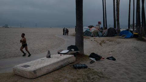 A man jogs past a mattress as several homeless people mingle next to their encampment set up along the boardwalk in the Venice neighborhood of Los Angeles, Tuesday, June 29, 2021. The proliferation of homeless encampments on Venice Beach has sparked an outcry from residents and created a political spat among Los Angeles leaders. (AP Photo/Jae C. Hong)