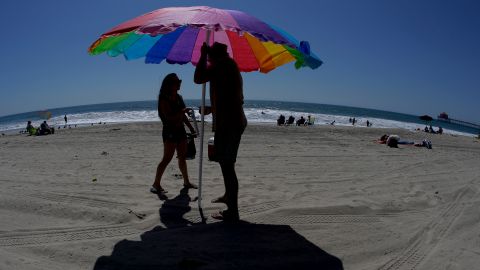 In this photo taken with a fisheye lens, Merissa Rocha, left, of Anaheim Calif., and Celso Arreola, of Los Angeles, plant their beach umbrella on the sand in an effort to avoid the ongoing southern California heat wave, Monday, Sept. 15, 2014, in Huntington Beach, Calif. Southern California is roasting in triple-digit temperatures and forecasters say the heat wave will continue at least another day. (AP Photo/Chris Carlson)