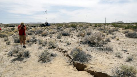 FILE - In this July 7, 2019 file photo, a visitor takes a photo of a crack in the ground following recent earthquakes near Ridgecrest, Calif. The Naval Air Weapons Station China Lake military base nearby remains closed to non-essential personnel as damage assessments continue following last week's powerful earthquakes in the area. (AP Photo/Marcio Jose Sanchez, File)