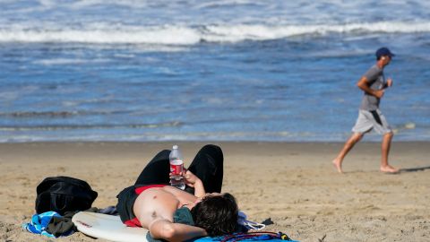 A surfer rests on his board as a jogger passes on Wednesday, May 13, 2020, in Manhattan Beach, Calif. Los Angeles County reopened its beaches Wednesday in the latest cautious easing of coronavirus restrictions that have closed most California public spaces and businesses for nearly two months. (AP Photo/Ashley Landis)