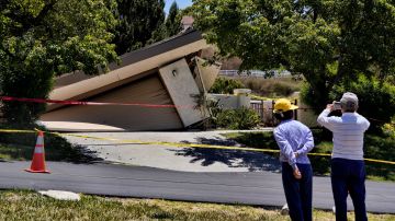 Neighborhood residents stop to take a photo of a damaged house in Rolling Hills Estates on the Palos Verdes Peninsula in Los Angeles County, on Monday, July 10, 2023. A dozen homes torn apart by earth movement on Southern California's Palos Verdes Peninsula during the weekend are likely to fall into an adjacent canyon. The homes were hastily evacuated by firefighters Saturday when cracks began appearing in structures and the ground. (AP Photo/Richard Vogel)