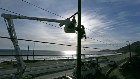 FILE - In this Nov. 13, 2018 file photo, Southern California Edison crews work to replace burned power poles and lines destroyed by the Woolsey Fire on Pacific Coast Highway in Malibu, Calif. SCE wants to spend $582 million to cover some power lines and deploy cameras in areas at high risk for wildfires. Officials from the utility shared plans with legislative staff on Monday, Dec. 10, 2018 as the utility works on clean up and repair from the Woolsey Fire last month. (AP Photo/Reed Saxon, File)