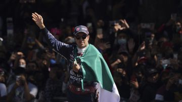 Mexican Formula One Red Bull driver Sergio "Checo" Perez waves as he holds his nation's flag after an exhibition race along Paseo de la Reforma ahead of this weekend's Mexico Grand Prix in Mexico City, Wednesday, Nov. 3, 2021. (AP Photo/Fernando Llano)