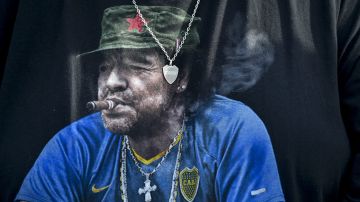 A Boca Juniors fan wears a T-shirt featuring the late soccer star Diego Maradona smoking a cigar and donning a red star beret, during an Argentine soccer league match against River Plate at La Bombonera stadium in Buenos Aires, Argentina, Saturday, Sept. 21, 2024.(AP Photo/Gustavo Garello)