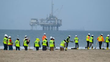 FILE - Workers in protective suits continue to clean the contaminated beach with a platform in the background in Huntington Beach, Calif., on Oct. 11, 2021. The owner of an underwater oil pipeline that spilled some 25,000 gallons of crude into the ocean off Southern California will pay nearly $1 million in cleanup costs. The Orange County Board of Supervisors on Tuesday, July 26, 2022 agreed to accept a proposed claim settlement with Amplify Energy Corp. over the costs of dealing with last October’s spill off Huntington Beach. (AP Photo/Ringo H.W. Chiu, File)