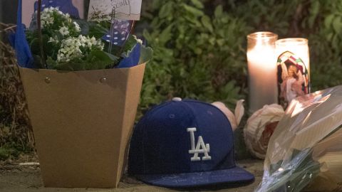 Los Angeles Dodgers fans pay their respects to broadcaster Vin Scully with baseball caps and flowers left next to a street sign bearing his name along Vin Scully Way at the entrance to Dodger Stadium in Los Angeles on Tuesday, Aug. 2, 2022. Scully, whose dulcet tones provided the soundtrack of summer while entertaining and informing Dodgers fans in Brooklyn and Los Angeles for 67 years, died Tuesday night, the team said. He was 94. (AP Photo/Damian Dovarganes)