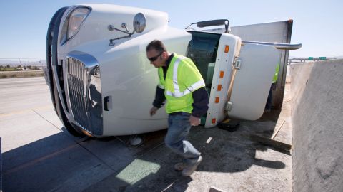 Morban Zarate, a response manager for Douple Barrel Environmental services walks around a truck blown over by strong winds Wednesday Feb. 2, 2011 near Rancho Cucamonga, Calif. The National Weather Service says winds gusts of up to 80 mph could blow through some areas in southern California, including the Cajon Pass, a heavily-traveled truck route through the mountains east of Los Angeles.(AP Photo/Nick Ut)