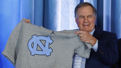 New North Carolina football coach Bill Belichick holds up a UNC branded sleeveless hoodie presented to him during an NCAA college football press conference announcing his hiring, Thursday, Dec. 12, 2024, in Chapel Hill, N.C. (AP Photo/Ben McKeown)