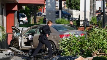 A Los Angeles Police Department officers assess an accident near downtown Los Angeles on Thursday, Oct. 6, 2016. The traffic accident left a vehicle overturned on a sidewalk and another smashed-up car in the drive-thru lane of a fast-food restaurant. (AP Photo/Richard Vogel)