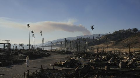 A person walks amidst debris as smoke rises from the Palisades Fire on Friday, Jan. 10, 2025, in the Pacific Palisades section of Los Angeles. (AP Photo/John Locher)