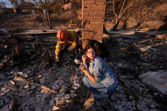 Ella Venne sostiene una taza que encontró entre los restos de la casa de su familia destruida por el incendio de Eaton mientras busca con el capitán del Departamento de Bomberos de Glendale, Chris Jernegan, a la izquierda, y su esposa Alison en Altadena.