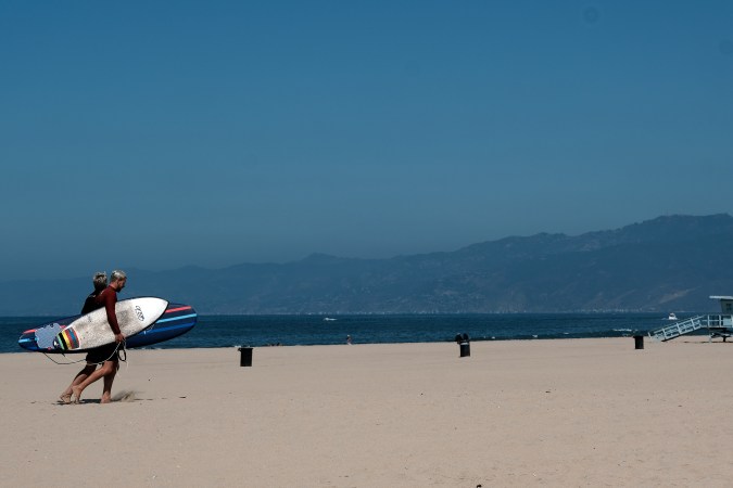 Surfers walk from the water along a closed and empty Venice beach on Friday, July 3, 2020 in Los Angeles. The Los Angeles County Department of Public Health has ordered all L.A. County beaches closed from July 3 through July 6, to prevent dangerous crowding that results in the spread of deadly COVID-19. California's governor is urging people to wear masks and skip Fourth of July family gatherings as the state's coronavirus tally rises. (AP Photo/Richard Vogel)