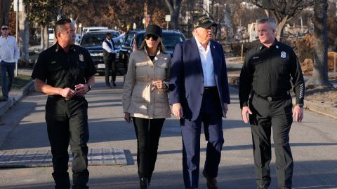 El presidente Trump y la primera dama Melania Trump caminan con Jason Hing, jefe adjunto de servicios de emergencia del Departamento de Bomberos de Los Ángeles, a la izquierda, y el capitán Jeff Brown, jefe de la Estación 69, por Pacific Palisades.