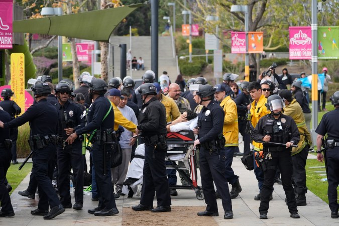Los Angeles riot police officers assist paramedics evacuating an injured high school student after a fist fight broke among students at a rally to stop President Trump's mass deportations and demand immigration reform at Grand Park in downtown Los Angeles on Friday, Feb. 7, 2025. (AP Photo/Damian Dovarganes)