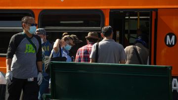 Los Angeles Metro commuters board a bus in Los Angeles on Thursday, May 14, 2020. Leaving home in Los Angeles now requires bringing a face covering, part of the price for reopening more businesses and activities in America's second-largest city. Mayor Eric Garcetti said everyone must carry the coverings when they go outdoors and wear them when they are around people from outside their households. (AP Photo/Damian Dovarganes)