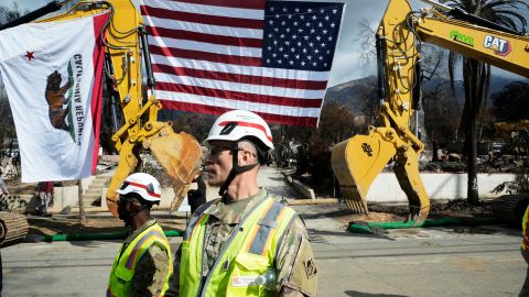 Col. Eric Swenson, center, of the U.S. Army Corps of Engineers, stands in front of a U.S. and California flag before a visit by California Gov. Gavin Newsom to an area affected by the Eaton Fire Tuesday, Feb. 11, 2025, in Altadena, Calif. (AP Photo/Damian Dovarganes)