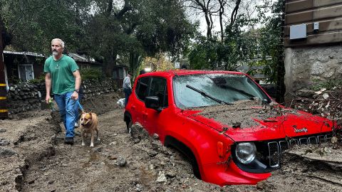 A resident and their dog walk past a vehicle partially submerged in mud after a storm Friday, Feb. 14, 2025, in Sierra Madre, Calif. (AP Photo/Eugene Garcia)