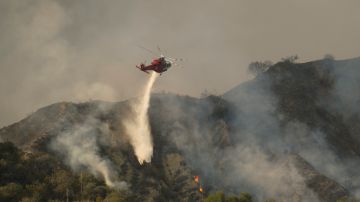 A firefighting helicopter drops water on a brush fire scorching at least 100 acres in the Pacific Palisades area of Los Angeles Saturday, May 15, 2021. (AP Photo/Ringo H.W. Chiu)