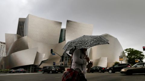 A morning commuter shields herself from the rain as she walks past the Walt Disney Concert Hall in downtown Los Angeles, Friday, May 6, 2016. Forecasters say a cold slow-moving storm packing an unusually high volume of moisture will douse the area and may trigger thunderstorms. (AP Photo/Nick Ut)