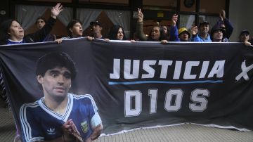 Fans of the late soccer star Diego Maradona hold a banner that reads in Spanish "Justice for God" outside the court where members of the medical team that treated Maradona go on trial for alleged homicide by negligence in San Isidro on the outskirts of Buenos Aires, Argentina, Tuesday, March 11, 2025. (AP Photo/Natacha Pisarenko)
