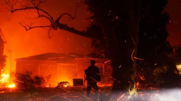 A person tries to hose down embers from the Palisades Fire in the Pacific Palisades neighborhood of Los Angeles, Tuesday, Jan. 7, 2025. (AP Photo/Etienne Laurent)