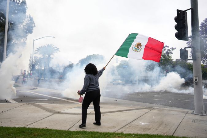 A woman waves a Mexican flag amidst tear gas from law enforcement during a protest in Paramount, Calif., Saturday, June 7, 2025, after federal immigration authorities conducted operations. (AP Photo/Eric Thayer)