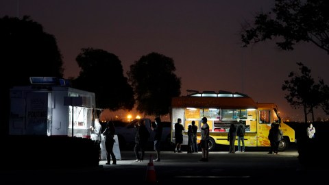 People stand in line to buy food from food trucks before watching "Ford v Ferrari" at a drive-in movie event at Ontario International Airport on Friday, June 19, 2020, in Ontario, Calif. The event was held in an airport parking lot that has been left unused due to fewer people traveling amid the coronavirus pandemic. (AP Photo/Ashley Landis)