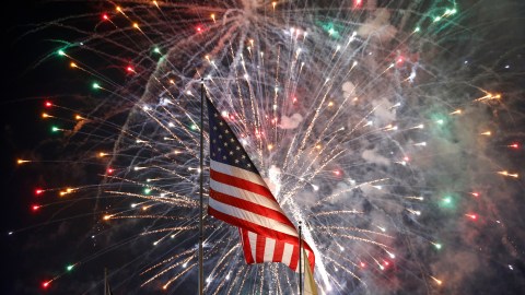 Fireworks explode behind a United States flag during a Fourth of July celebration at State Fair Meadowlands, Saturday, July 4, 2015, in East Rutherford, N.J. (AP Photo/Julio Cortez)