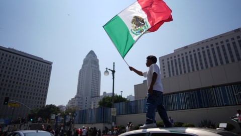A protester waves a Mexico national flag on top of a car near the metropolitan detention center, Monday, June 9, 2025, in downtown Los Angeles. (AP Photo/Eric Thayer)