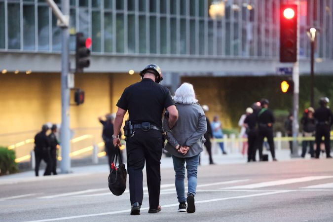 A law enforcement officer escorts a woman out of a protest after she was detained on Wednesday, June 11, 2025, in Los Angeles. (AP Photo/Ethan Swope)