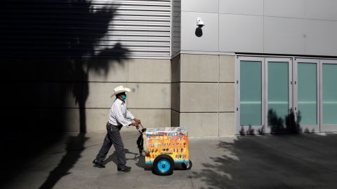 A street vendor wears a mask while working the downtown district Monday, March 30, 2020, in Los Angeles. Over the weekend, more people appeared to heed the message to stay home after beaches and many parks were closed by state and local officials following a swarm of visitors during the first weekend of the state's stay-at-home order in reaction to the coronavirus pandemic. (AP Photo/Marcio Jose Sanchez)