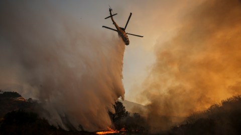 FILE- In this Sunday, July 24, 2016 file photo, a helicopter makes a drop on a wildfire near Placerita Canyon Road in Santa Clarita, Calif. The smoky fire tore through drought-ravaged brush that hadn't burned in decades amid a sweltering heat wave and exploded over the weekend. (AP Photo/Ringo H.W. Chiu/File)