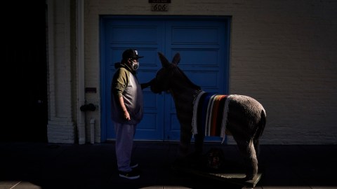 Jesus Hernandez, a merchant who owns a gift shop on Olvera Street that only opens on weekends due to the pandemic, waits for a key to store his uncle's life-size stuffed donkey, a photo prop named George, in downtown Los Angeles, Wednesday, Dec. 16, 2020. Olvera Street, known as the birthplace of Los Angeles, has been particularly hard hit by the coronavirus pandemic, with shops and restaurants closed and others barely hanging on. (AP Photo/Jae C. Hong)