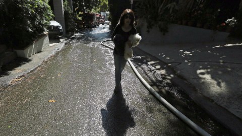 A woman walks through water on the street from fire trucks as she carries her two dogs back to her undamaged home on Portola Drive after a wildfire broke out in the Benedict Canyon area of Los Angeles Tuesday, June 12, 1018. Some residents evacuated their homes as more than 250 firefighters battled flames on the ground and from the air. (AP Photo/Reed Saxon)