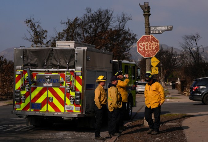 Members of the California Governor's Office of Emergency Services, Fire and Rescue Division, pause by a fire-cracked stop sign in a neighborhood destroyed by the Palisades Fire, Sunday, Jan. 19, 2025, in the Pacific Palisades neighborhood of Los Angeles. (AP Photo/Carolyn Kaster)