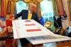 El presidente Trump sostiene gráficos mientras habla sobre la economía en el Despacho Oval en agosto de 2025.