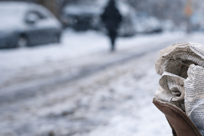 Botas de invierno apoyadas sobre la nieve con papel de diario dentro, un truco casero para aislar el frío en días de tormenta invernal.