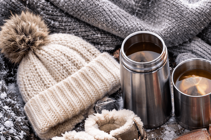 Ropa de abrigo, bebidas calientes y accesorios esenciales para soportar el frío extremo sobre una mesa con nieve.