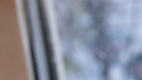 Persona con guantes de lana busca información sobre la nieve en Estados Unidos desde su celular frente a una ventana con nieve.