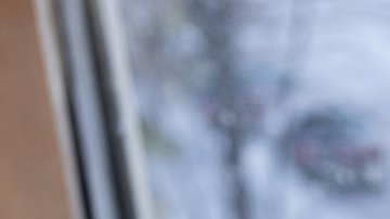 Persona con guantes de lana busca información sobre la nieve en Estados Unidos desde su celular frente a una ventana con nieve.