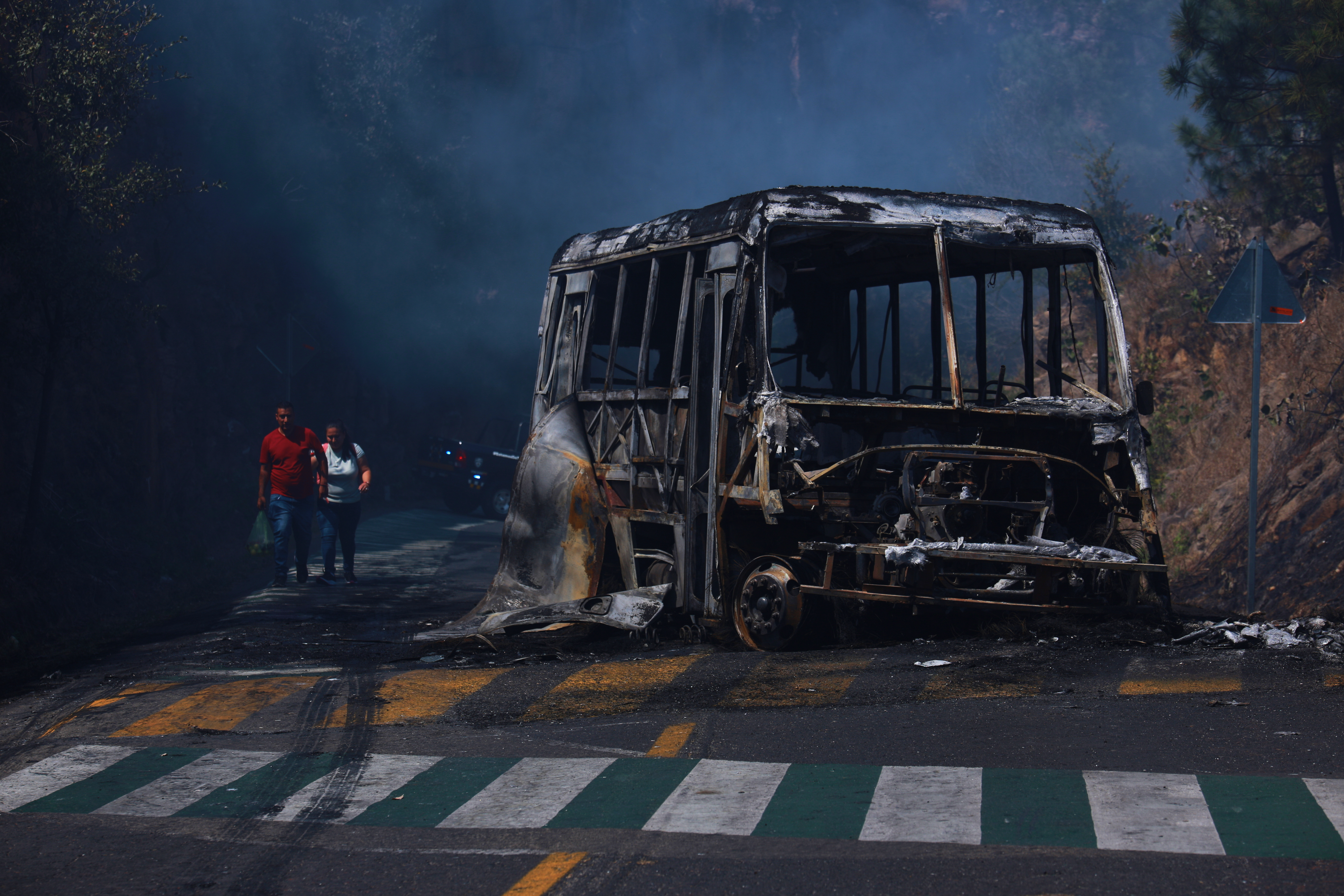 Peatones pasan junto a un vehículo calcinado tras ser incendiado en una carretera de Cointzio, Michoacán, México, el domingo 22 de febrero de 2026, tras la muerte del líder del Cártel Jalisco Nueva Generación, Nemesio Rubén Oseguera Cervantes, conocido como "El Mencho".
