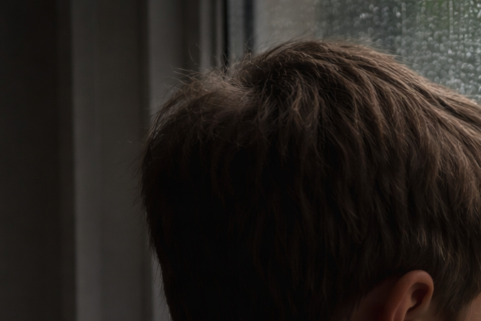 Niño observando por una ventana con lluvia, reflejando preocupación y tristeza en un entorno escolar